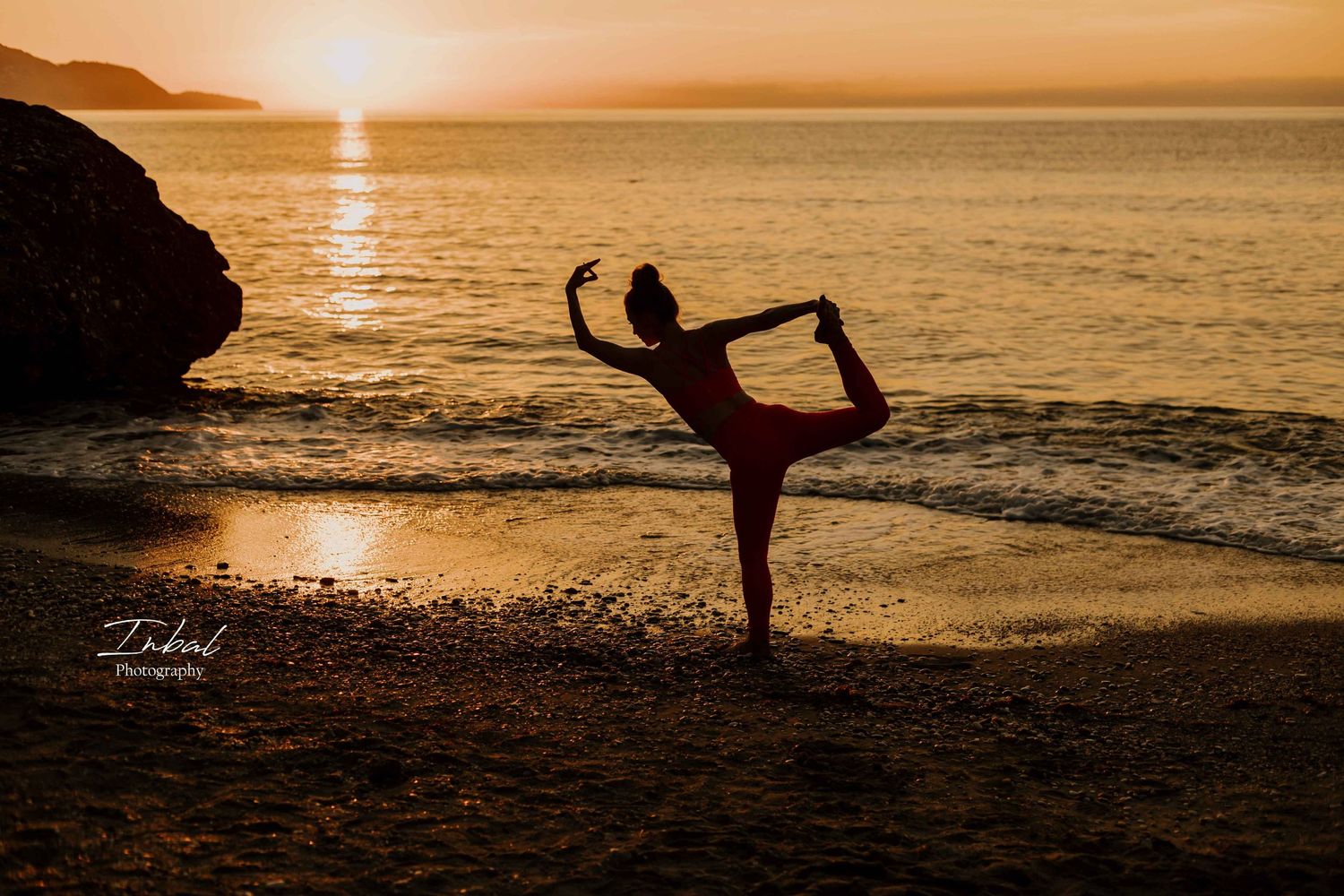 Silhouette of a woman in a yoga pose on the beach at sunrise, with a golden sun reflecting on the calm ocean waves.