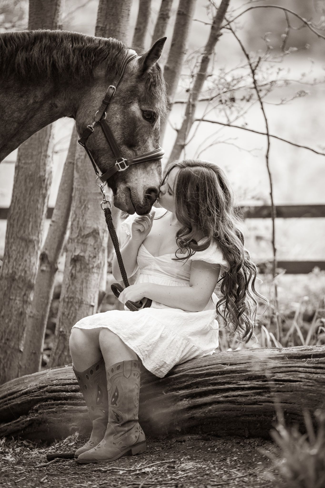 A gentle moment between a rider and dark horse with white blaze in a rustic stable setting, captured in black and white.