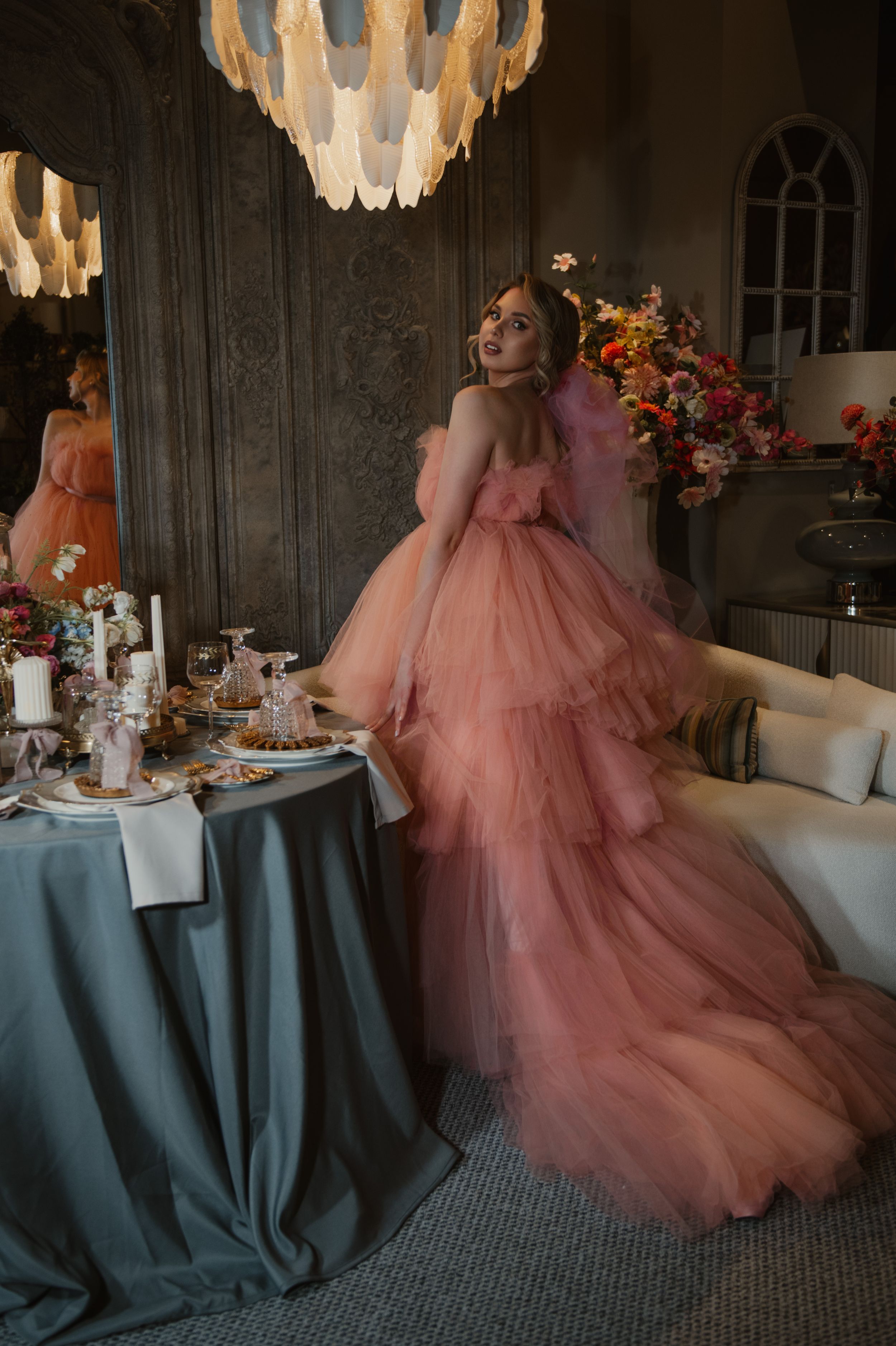 Elegant dining setup with teal tablecloths and pink floral decor under crystal chandeliers in a rustic wood-paneled room.