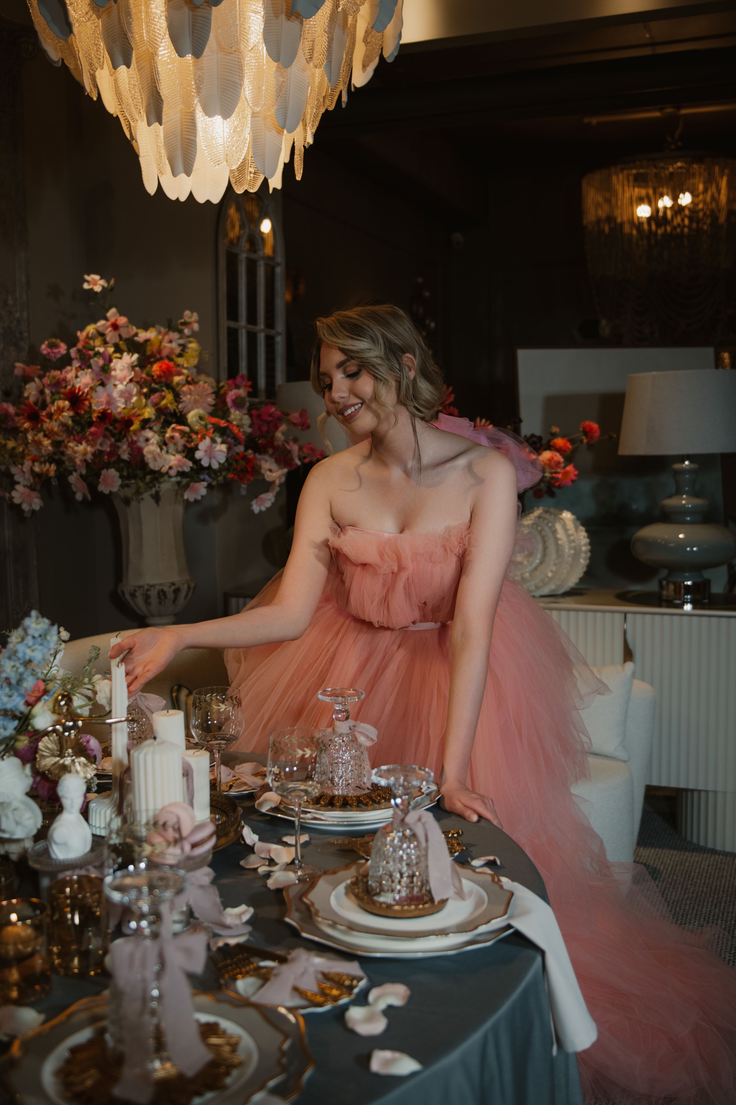 Elegant dining table setup with chandelier and pink tulle dress in a romantic indoor setting.