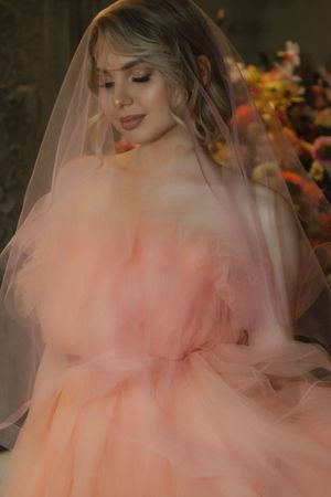 A bride wearing a soft peach tulle gown and veil poses with closed eyes in romantic lighting.
