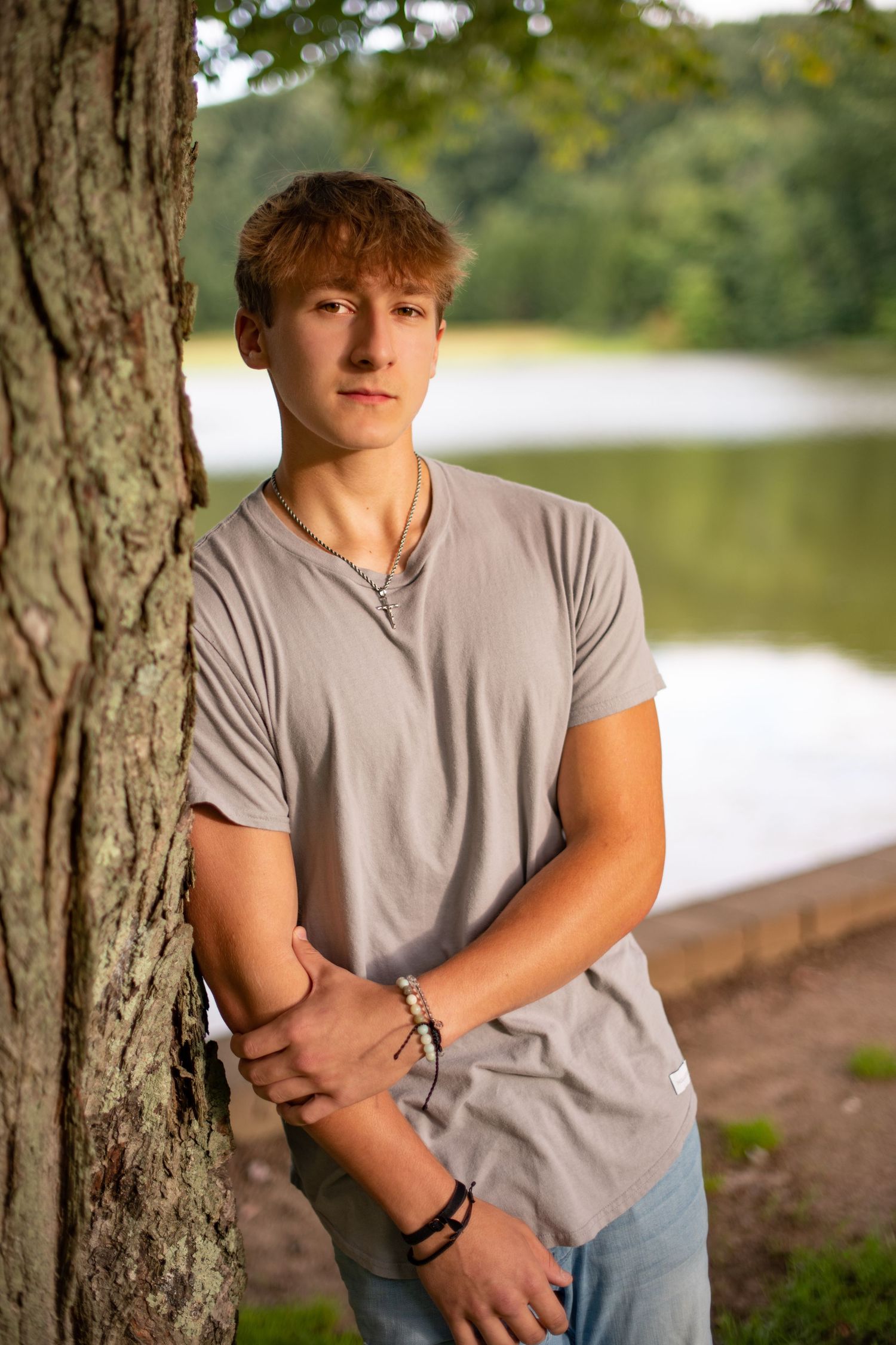 Someone sits peacefully on a wooden dock overlooking a serene lake surrounded by lush green forest.