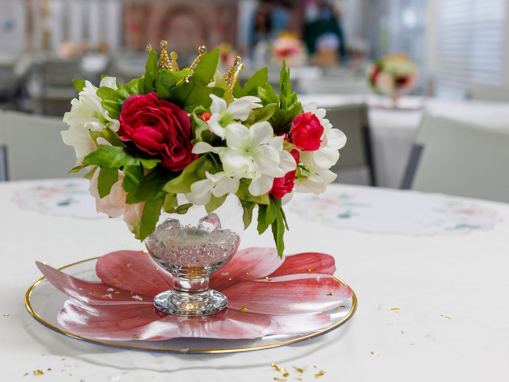 Elegant floral centerpiece with red roses and white flowers in a crystal vase on a decorative pink plate at a festive event.