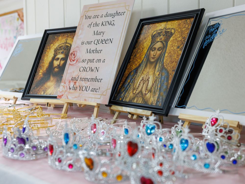 Catholic display with Virgin Mary icons, inspirational sign, and decorative toy crowns on a pink table.