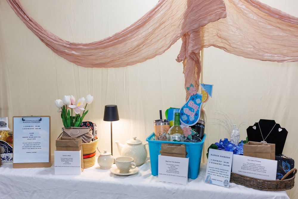 A decorated display table with white tablecloth, gift baskets, jewelry, tulips, and pink fabric draping at a charity auction event.