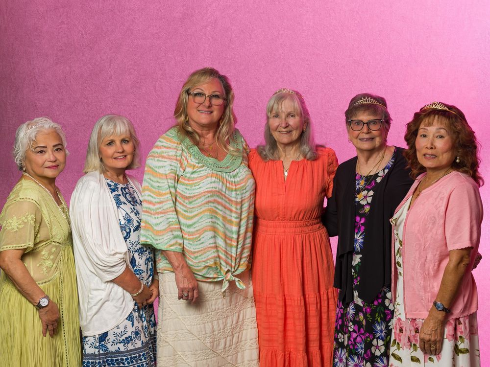 Six smiling women posing together in front of a pink background, wearing colorful outfits at a group gathering.