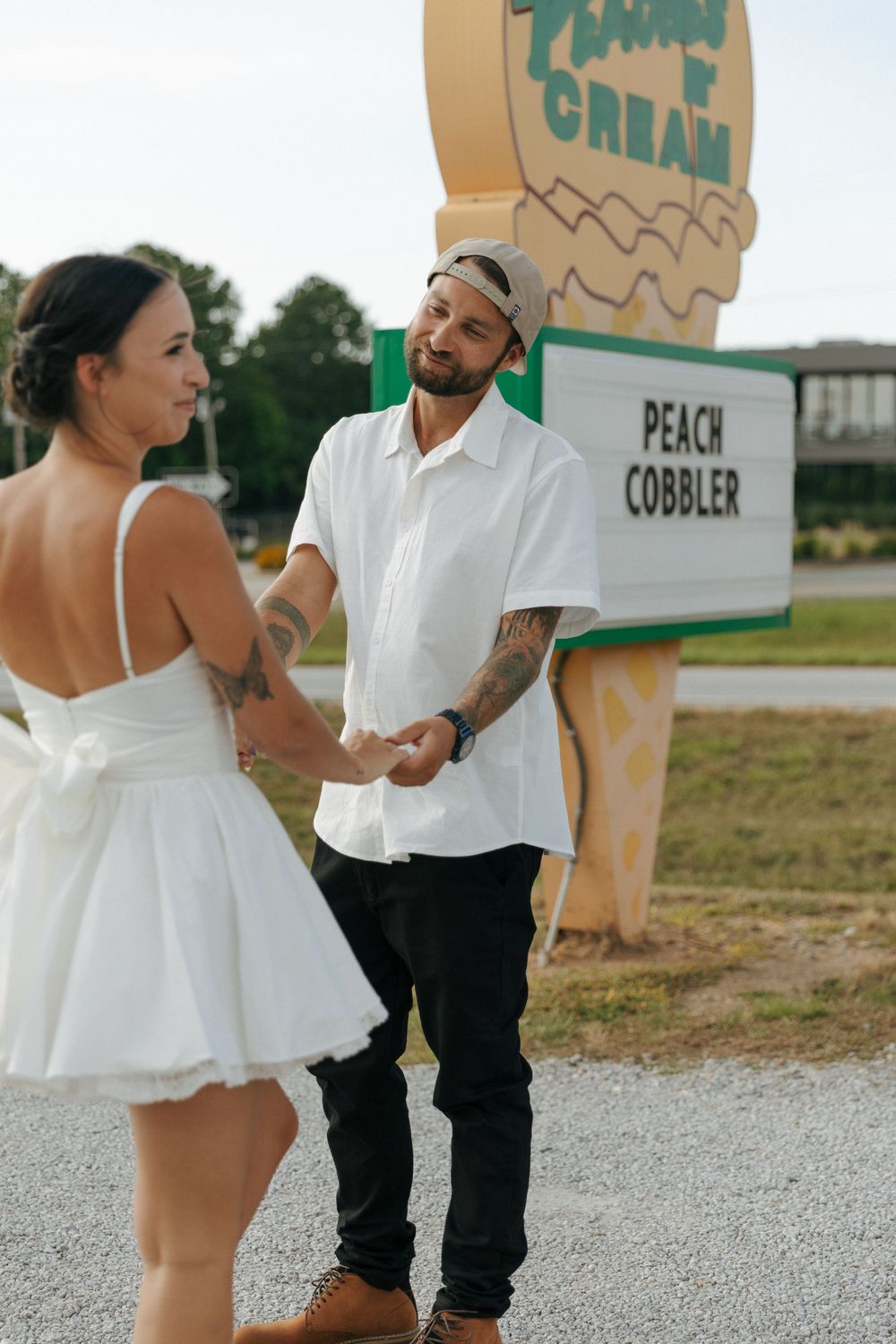 A couple shares a sweet moment in front of a large ice cream sign advertising Peach Cobbler flavor.