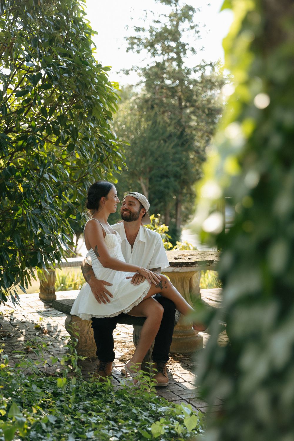 A romantic moment captured in a lush garden setting with sunlit greenery and a stone bench.
