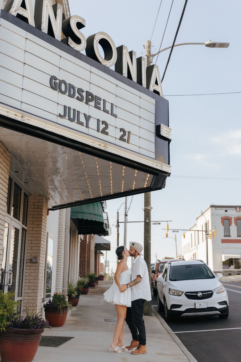 Couple stands beneath vintage Ansonia Theater marquee advertising Godspell performance on a cloudy day.