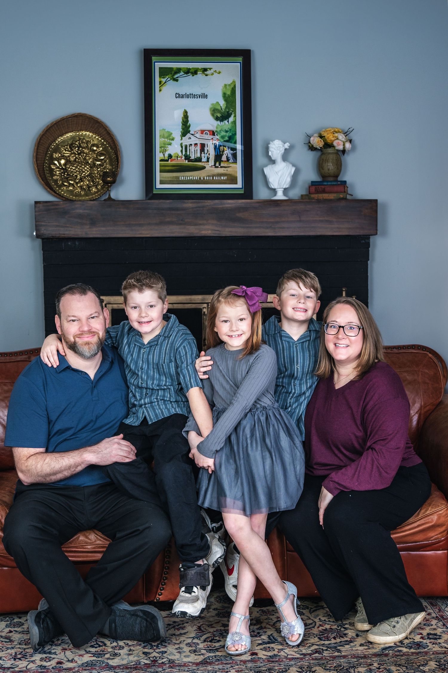 Family sitting together on a brown leather couch with decorative wall shelf display featuring artwork and decor above.