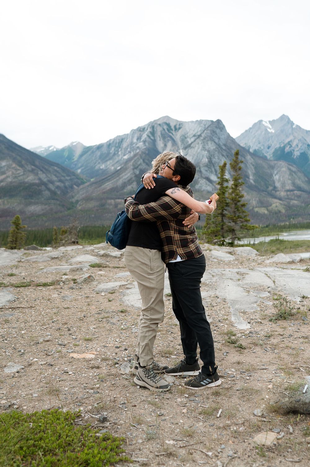Two people embrace in celebration with majestic Rocky Mountains in background.
