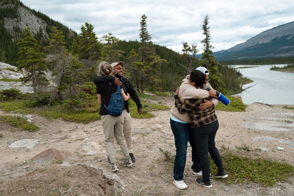 A group celebrates together on a rocky mountain overlook with a lake and mountains in the distance.