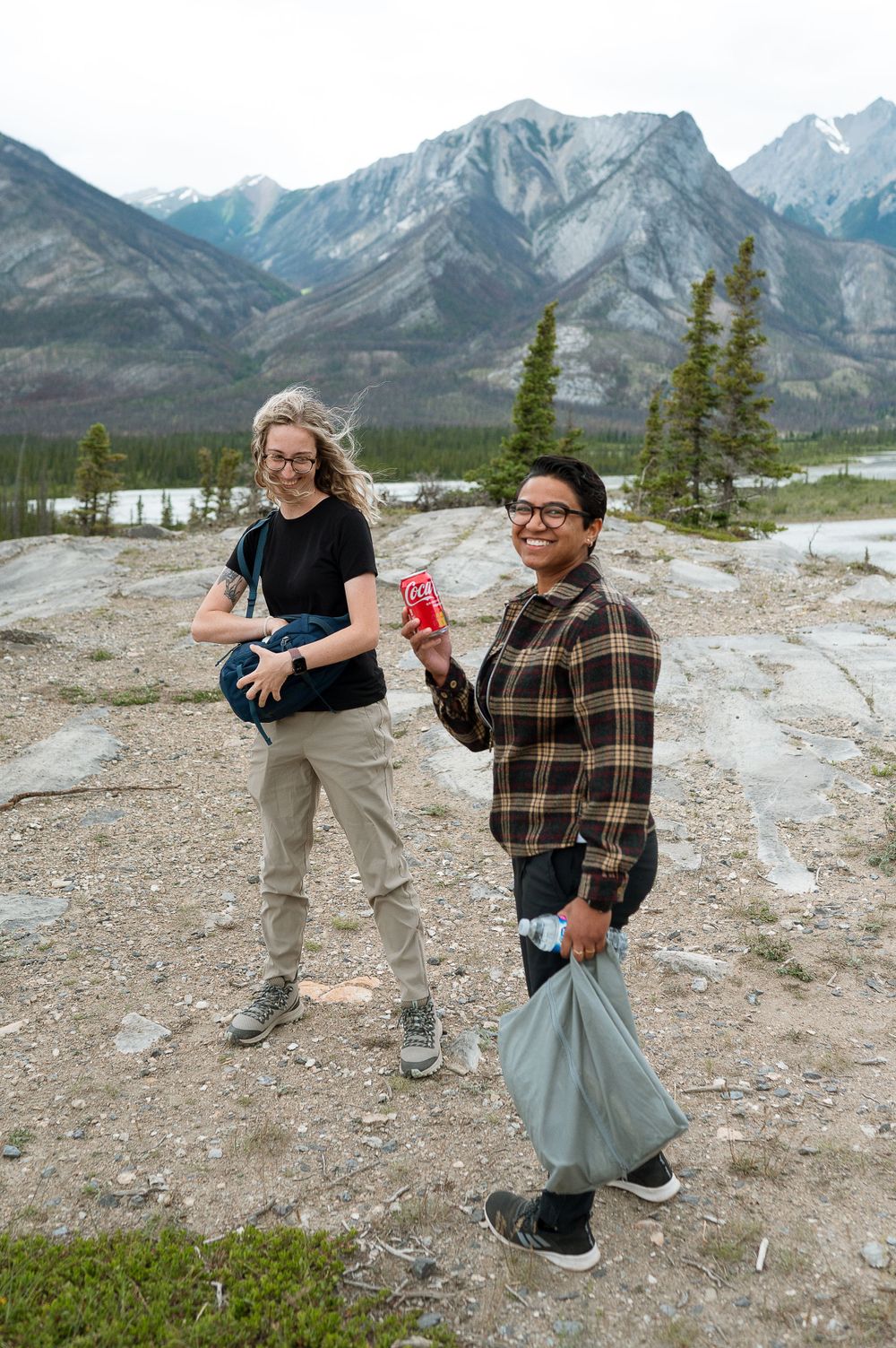 Two people sharing drinks with mountains and evergreen trees in the background.