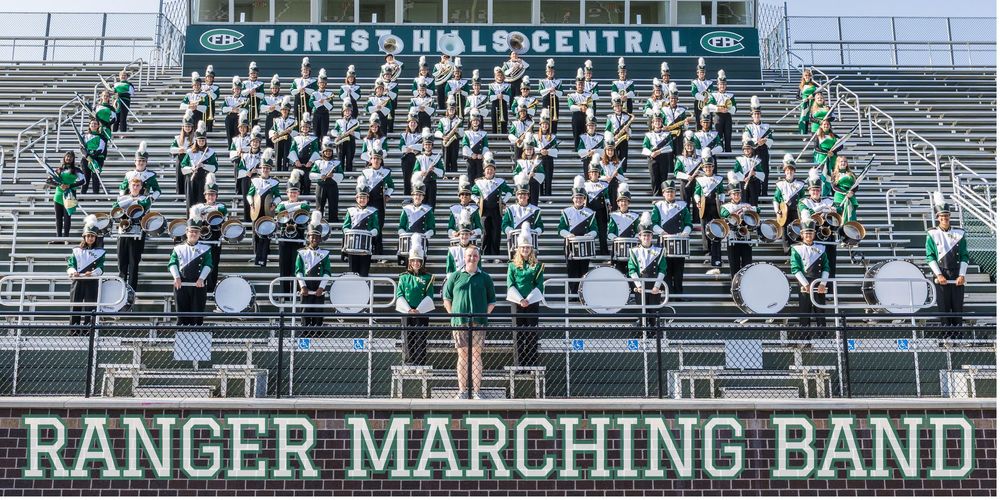 Forest Hills Central Ranger Marching Band poses in stadium bleachers in green and white uniforms.