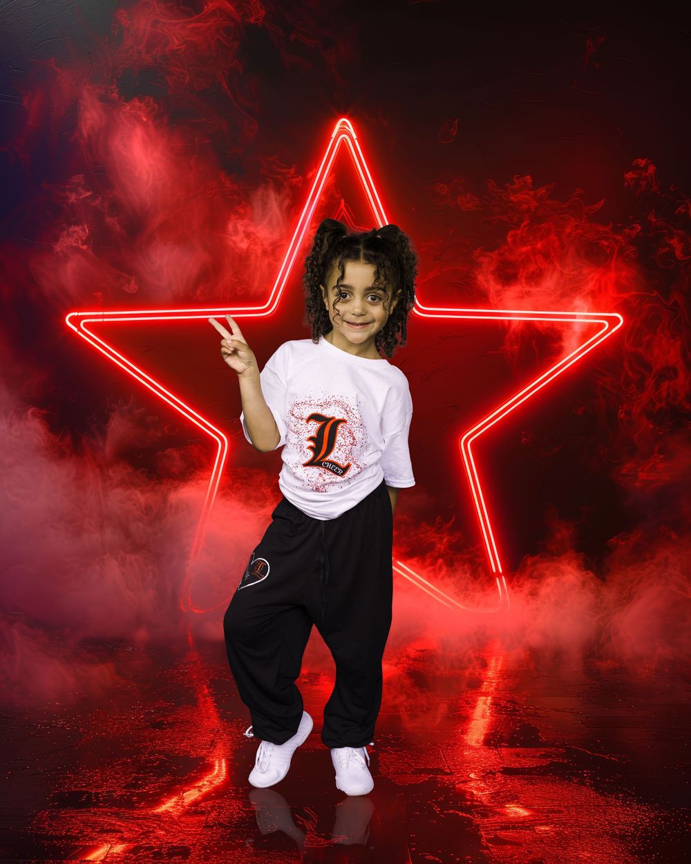 Young girl poses in front of red neon star with smoky background, wearing white graphic tee and black pants.