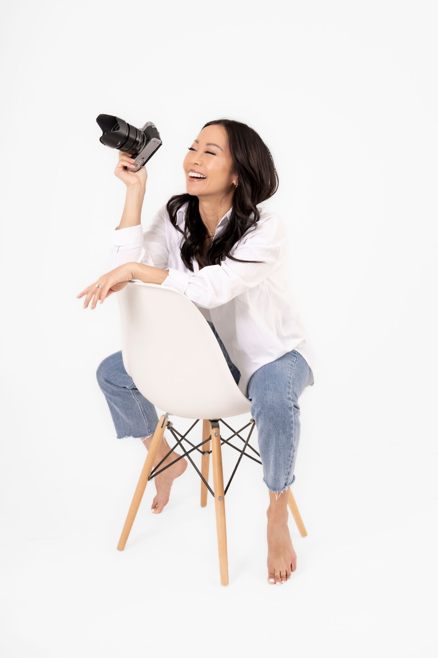 Woman in white shirt and jeans laughing while sitting on modern white chair.