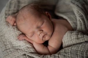 Peaceful sleeping newborn baby wrapped in textured grey fabric during a professional photography session.