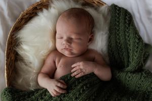 Newborn baby sleeping peacefully in basket with soft white fur and green knitted blanket.