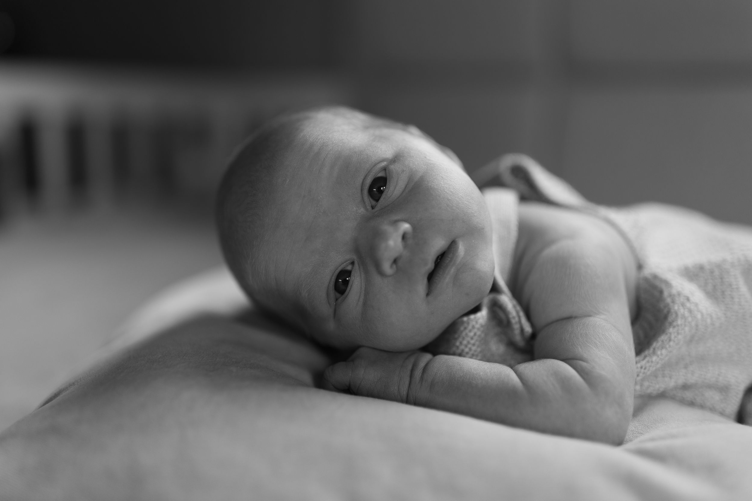 A black and white photograph of an infant lying on their side looking directly at the camera.