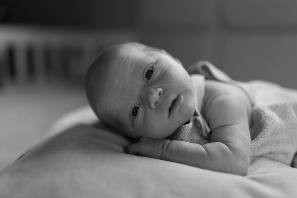 A black and white photograph of an infant lying on their side looking directly at the camera.