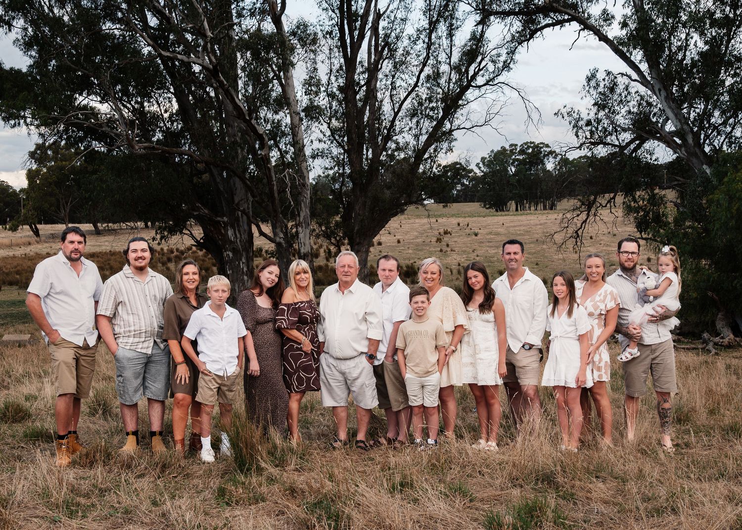 Extended family wearing coordinated white and neutral outfits poses together in rustic field setting.