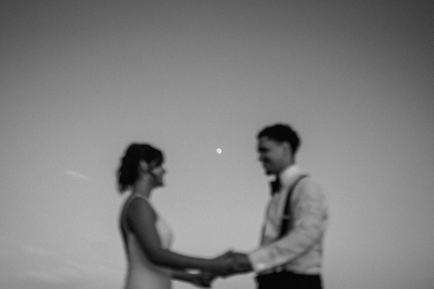 A couple holds hands in a romantic black and white photograph with a dreamy, blurred effect.