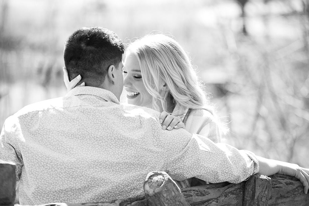Romantic black and white portrait of a couple sharing an intimate moment on a bench.