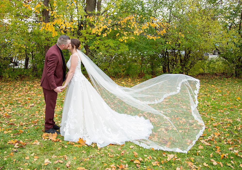 Autumn wedding photo with flowing veil and lace dress against colorful fall foliage.