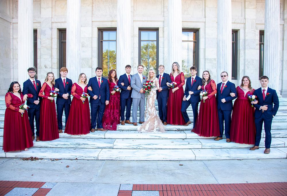 Wedding party poses on grand steps wearing burgundy and navy attire.