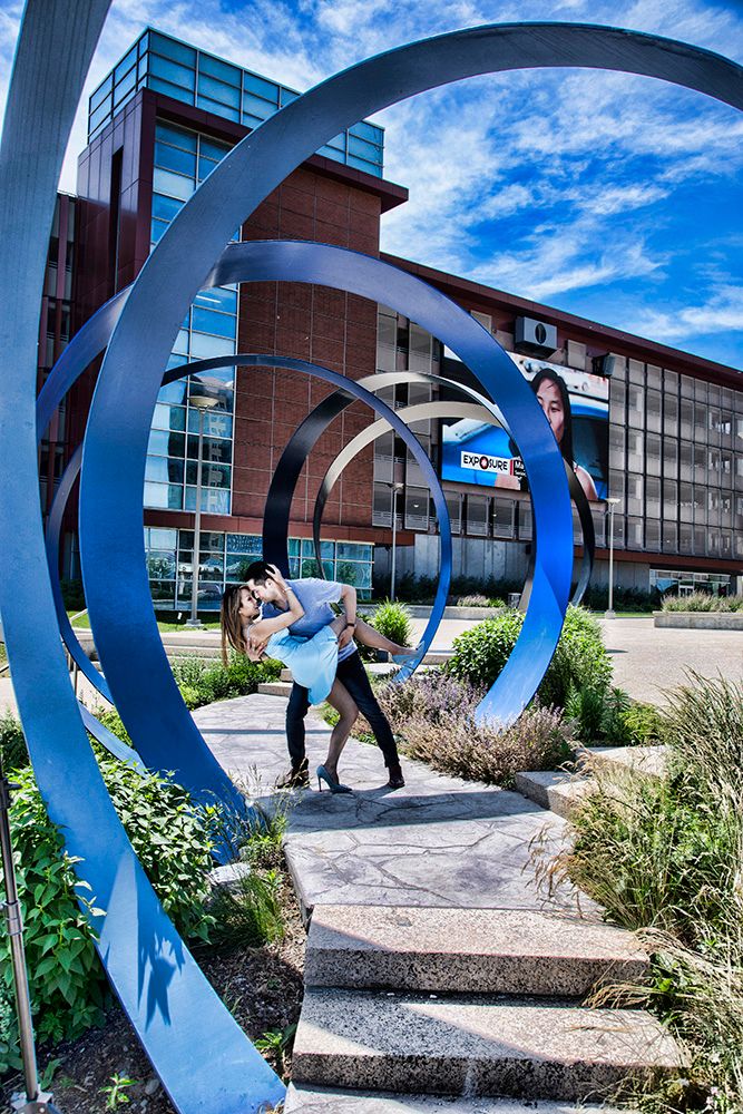 A wedding couple poses under a large blue spiral sculpture outside a modern building.