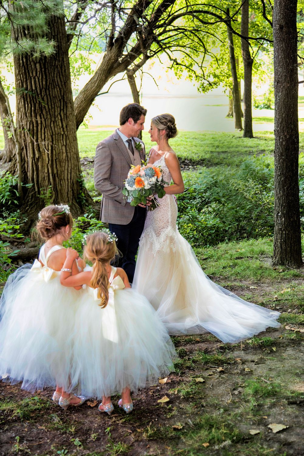 Wedding ceremony in wooded setting with flowing white dresses against natural greenery.