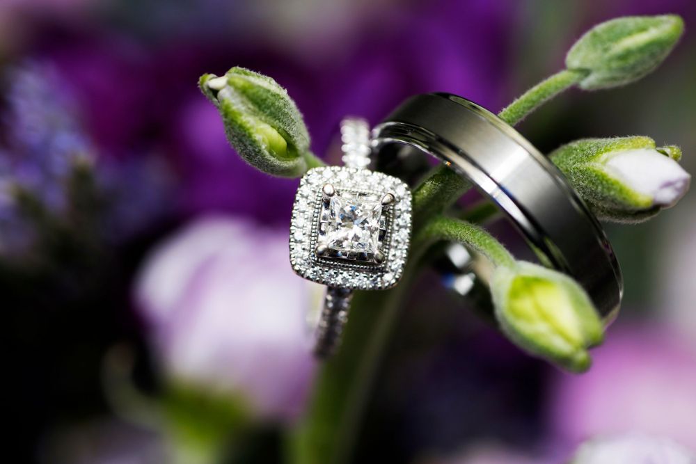 Wedding rings displayed on green buds with sparkling diamond engagement ring in focus.