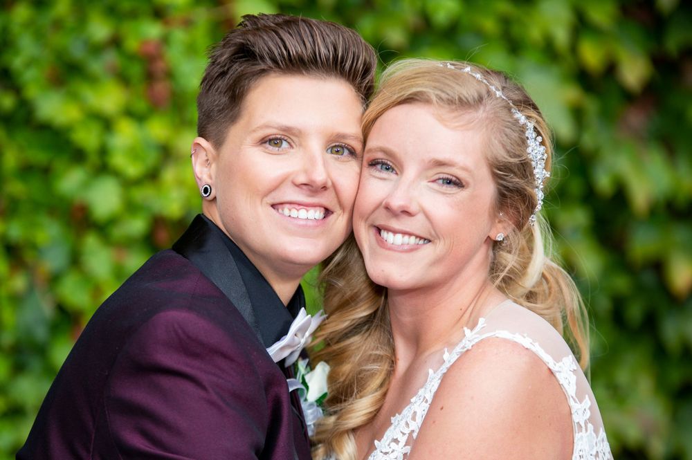 Wedding couple shares joyful moment against ivy-covered wall in formal attire.
