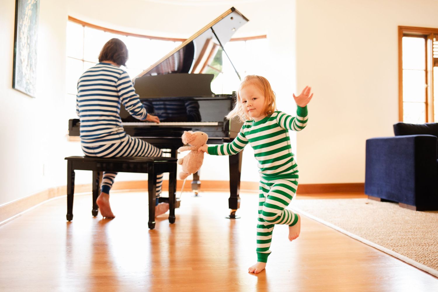 A joyful moment as music plays on a grand piano while a child in green striped pajamas dances in a bright room.