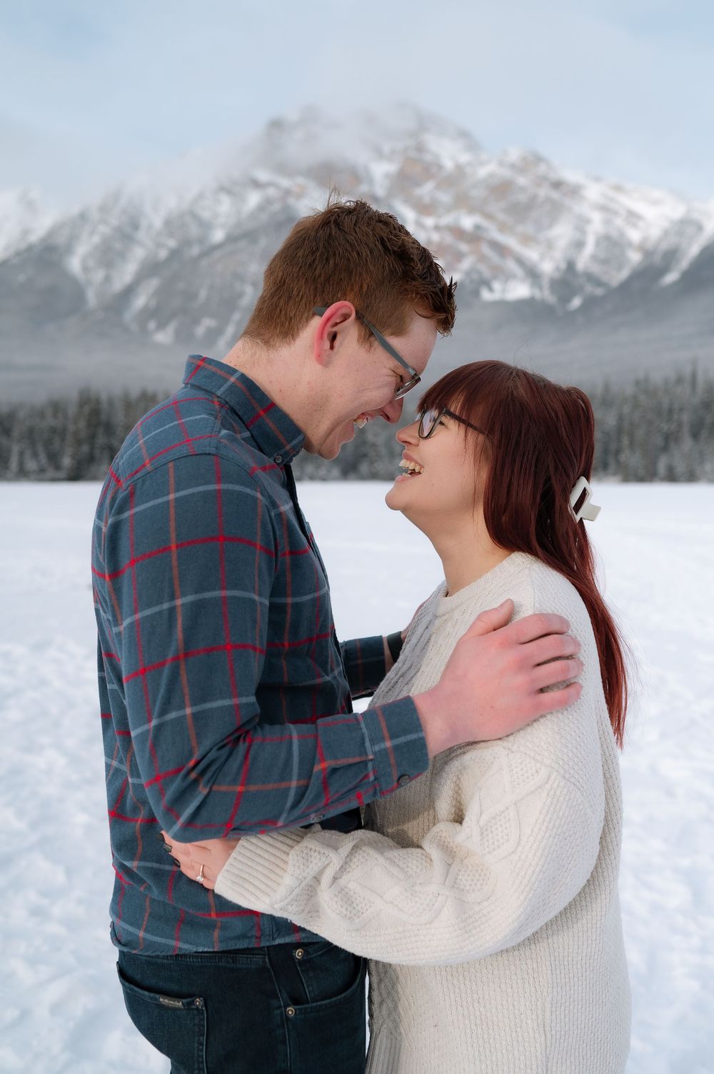 A romantic winter moment shared between a couple against a backdrop of snow-covered mountains.