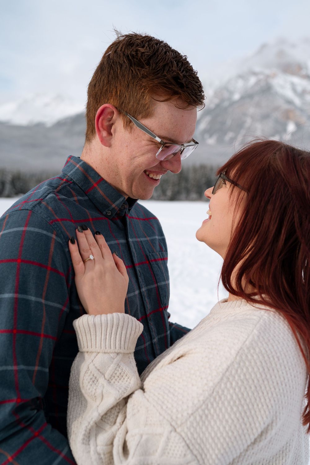 A couple shares a romantic moment in the snow with snow-capped mountains in the background.
