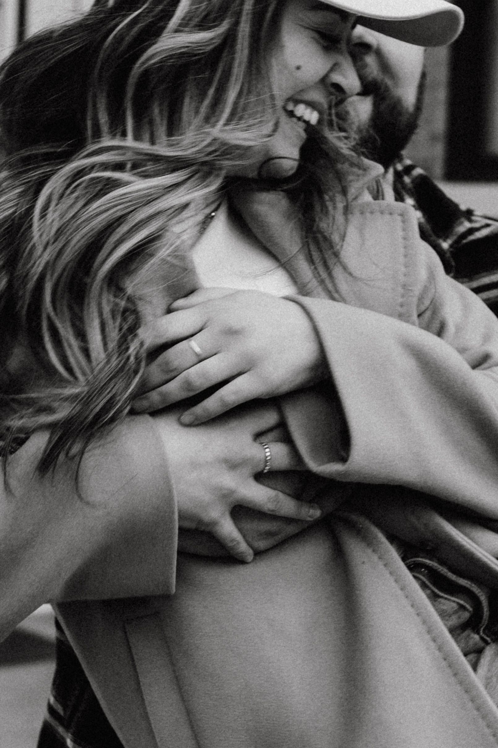 A romantic black and white close-up portrait of a couple embracing and laughing while wearing winter coats.