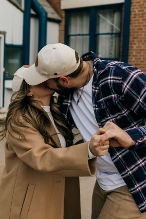 A couple in casual autumn attire sharing an intimate moment outdoors by a brick building.