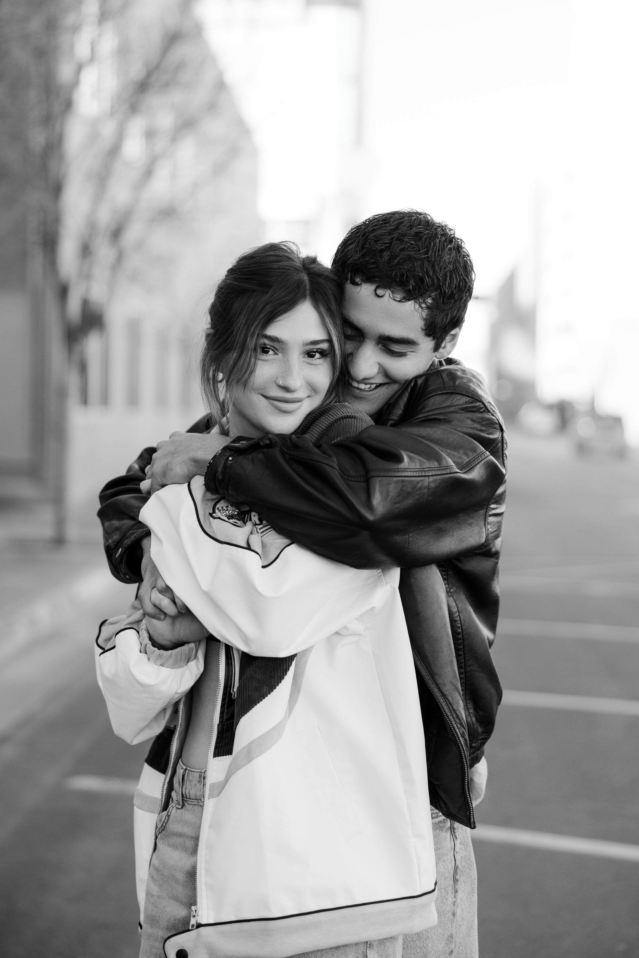 A romantic black and white photo of a couple embracing outdoors, with one wearing a white and black jacket.