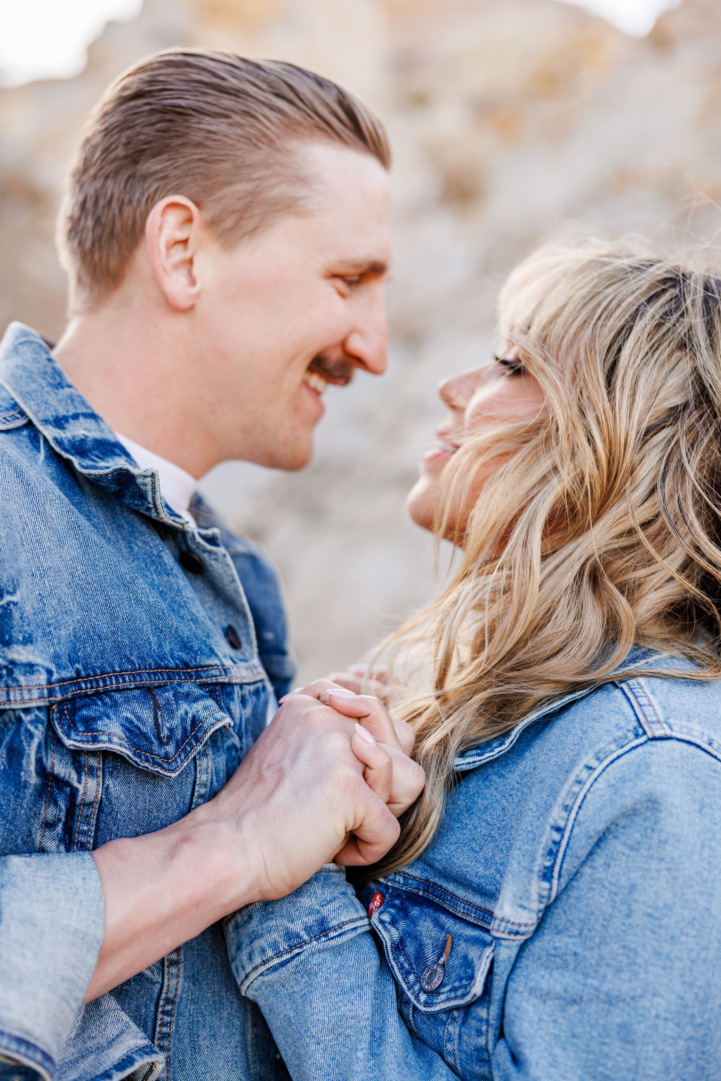 A romantic couple in matching denim jackets sharing a tender moment while gazing at each other and smiling.