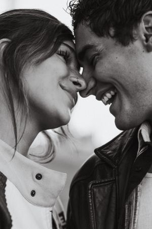A romantic black and white close-up photo of a couple touching foreheads and laughing together.