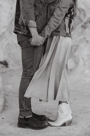Close-up view of two people embracing while wearing contrasting boots - western cowboy boots and dark casual boots.