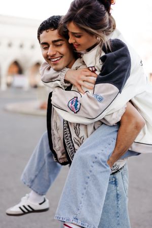A playful couple sharing a joyful moment outdoors, with one person wearing a NASA jacket and light denim jeans.