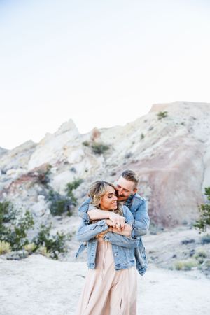 A couple embraces against a scenic backdrop of white and pink rock formations in a desert landscape.