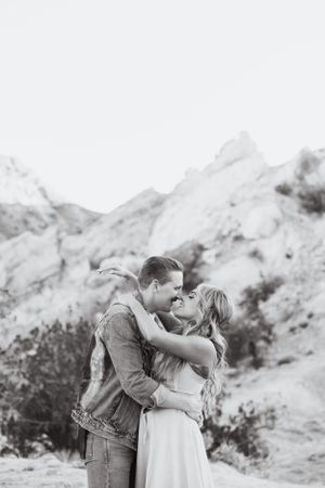 A romantic couple embraces against a dramatic mountainous backdrop in black and white.