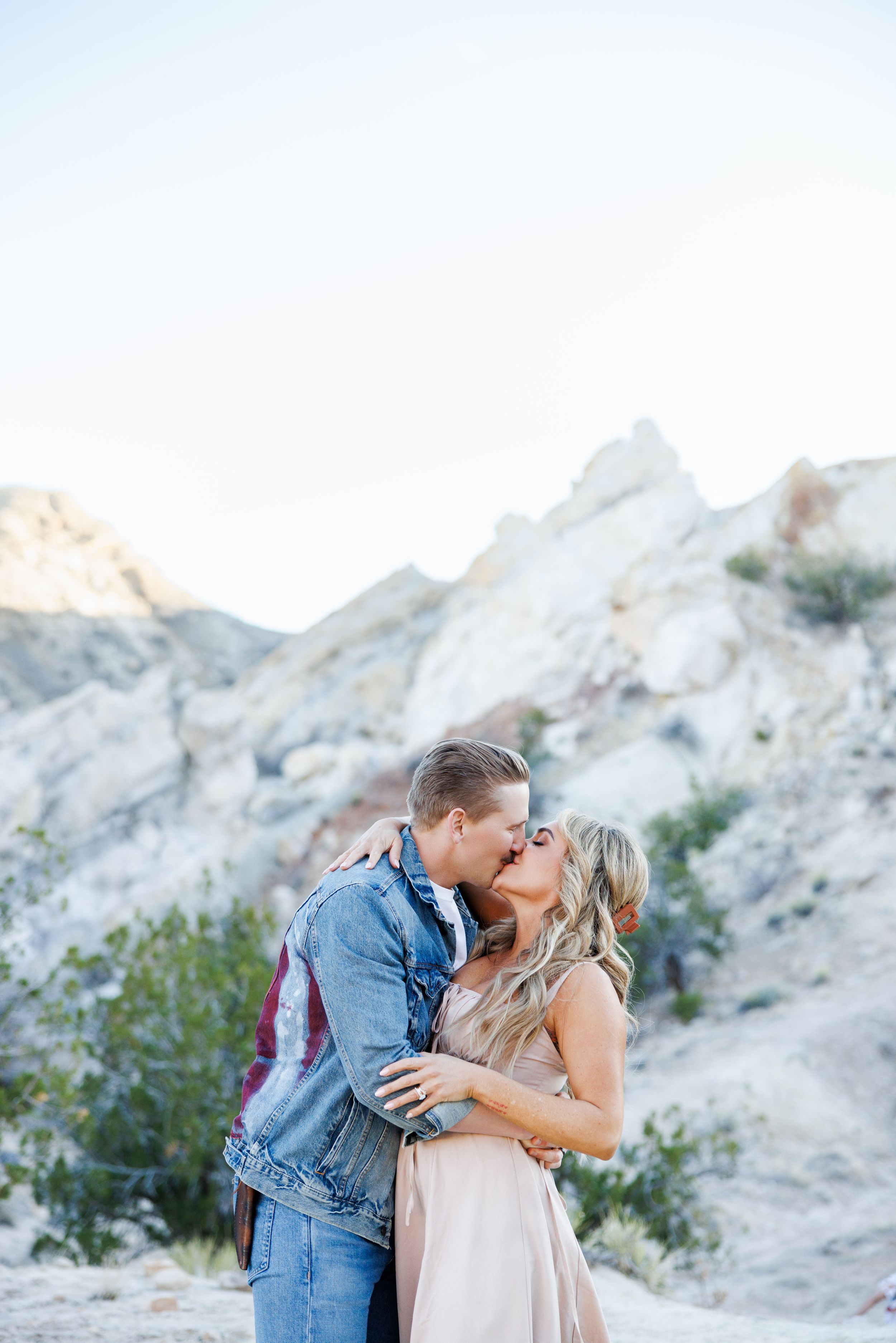 A romantic couple shares a tender moment against a backdrop of majestic white mountain cliffs during sunset.