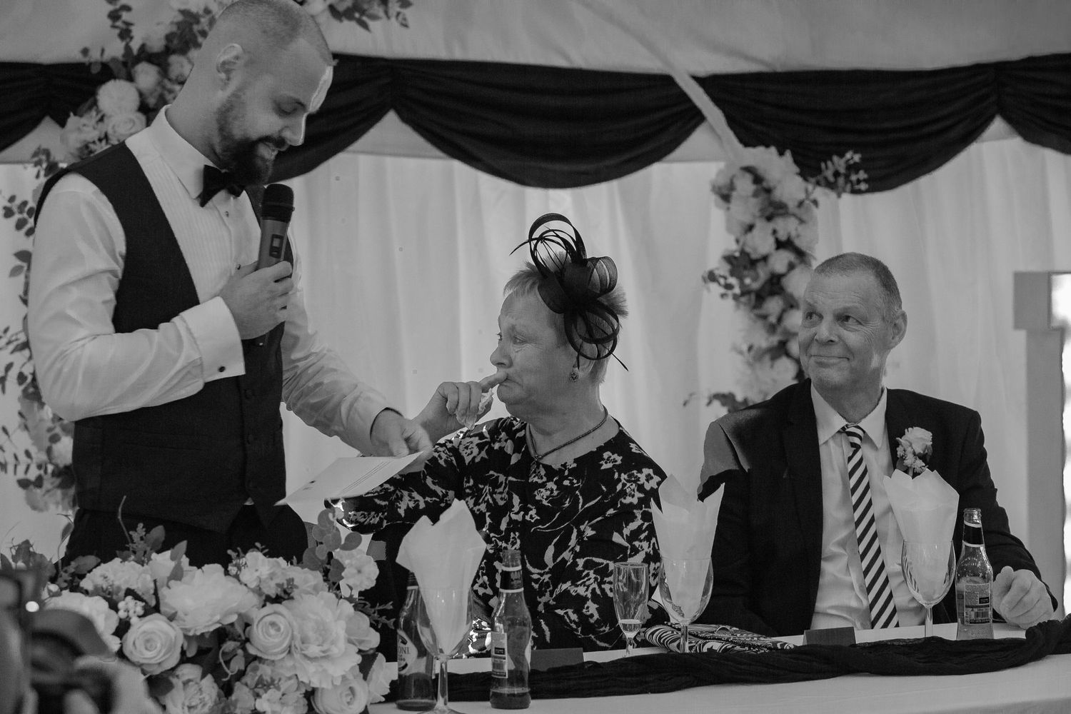 Black and white photo of wedding speeches at reception with elegant table settings.