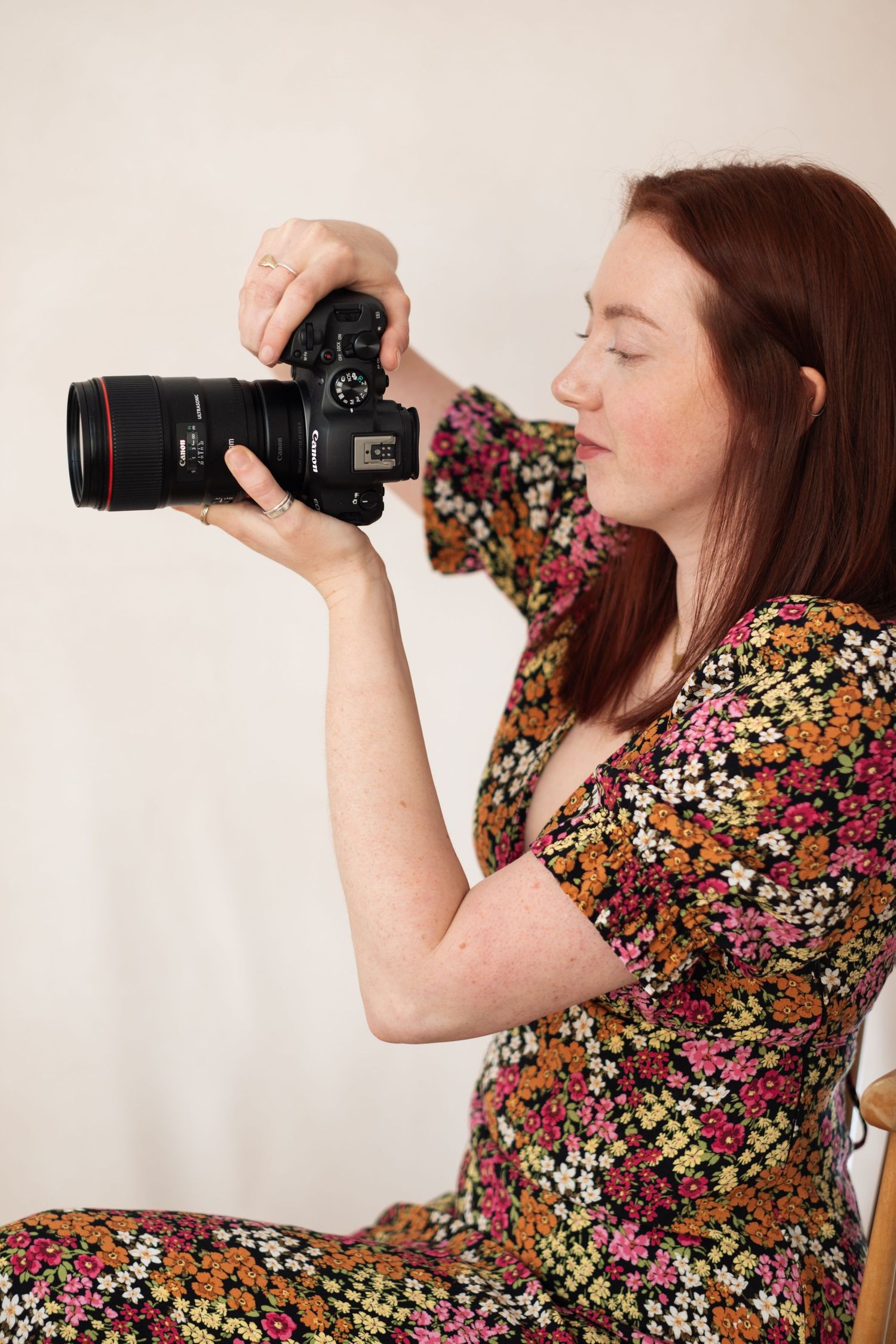 A portrait of a woman in a gingham dress touching her hair against a light background.
