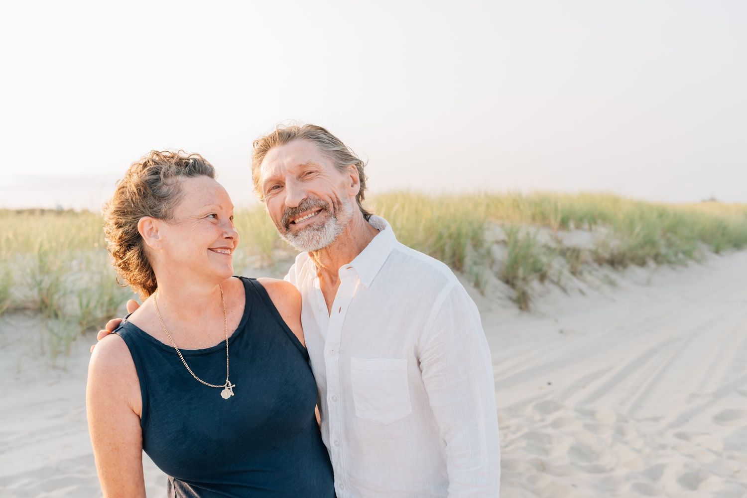 An older couple snuggle together standing close together on the beach in NJ.