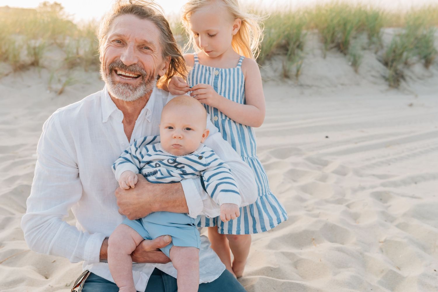 A grandfather kneels on the beach with his grandchildren while Lauren Marie photography captures the moment.